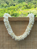 White double  tuberose lei hanging from wooden frame