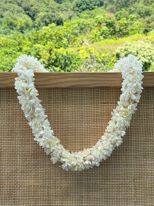White double  tuberose lei hanging from wooden frame
